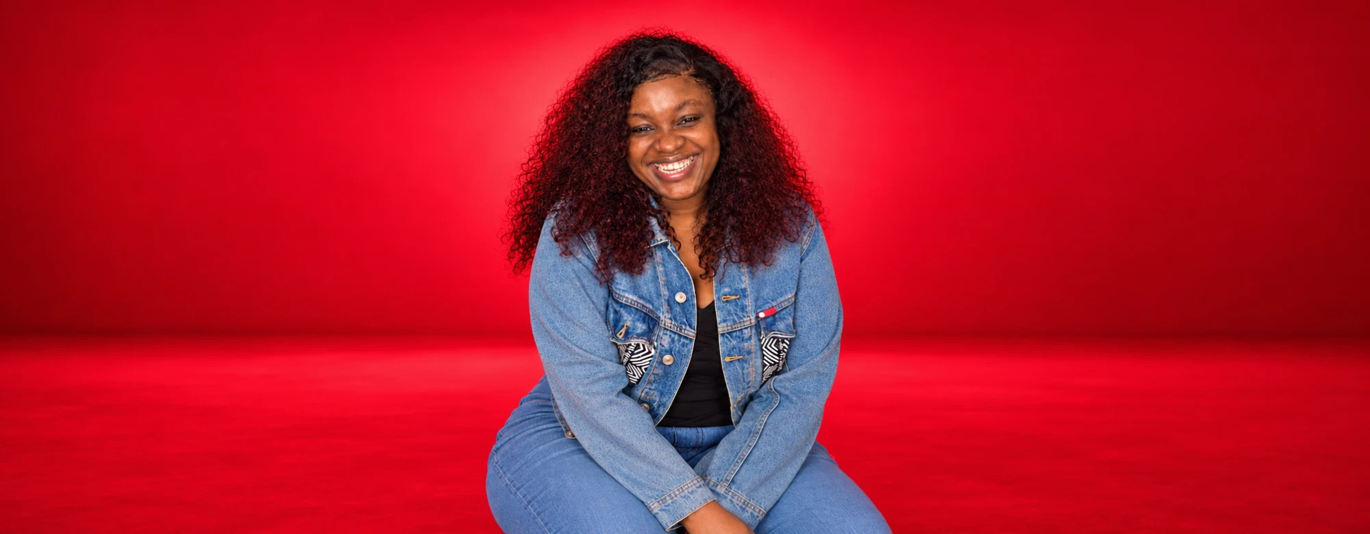 Yié Juku, assise, veste en jean sur fond rouge